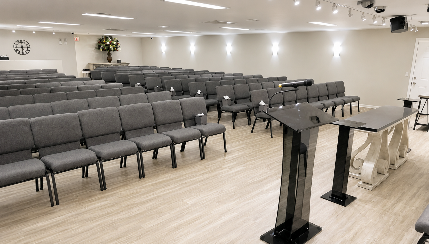 Empty room with rows of gray chairs facing a podium and presentation area