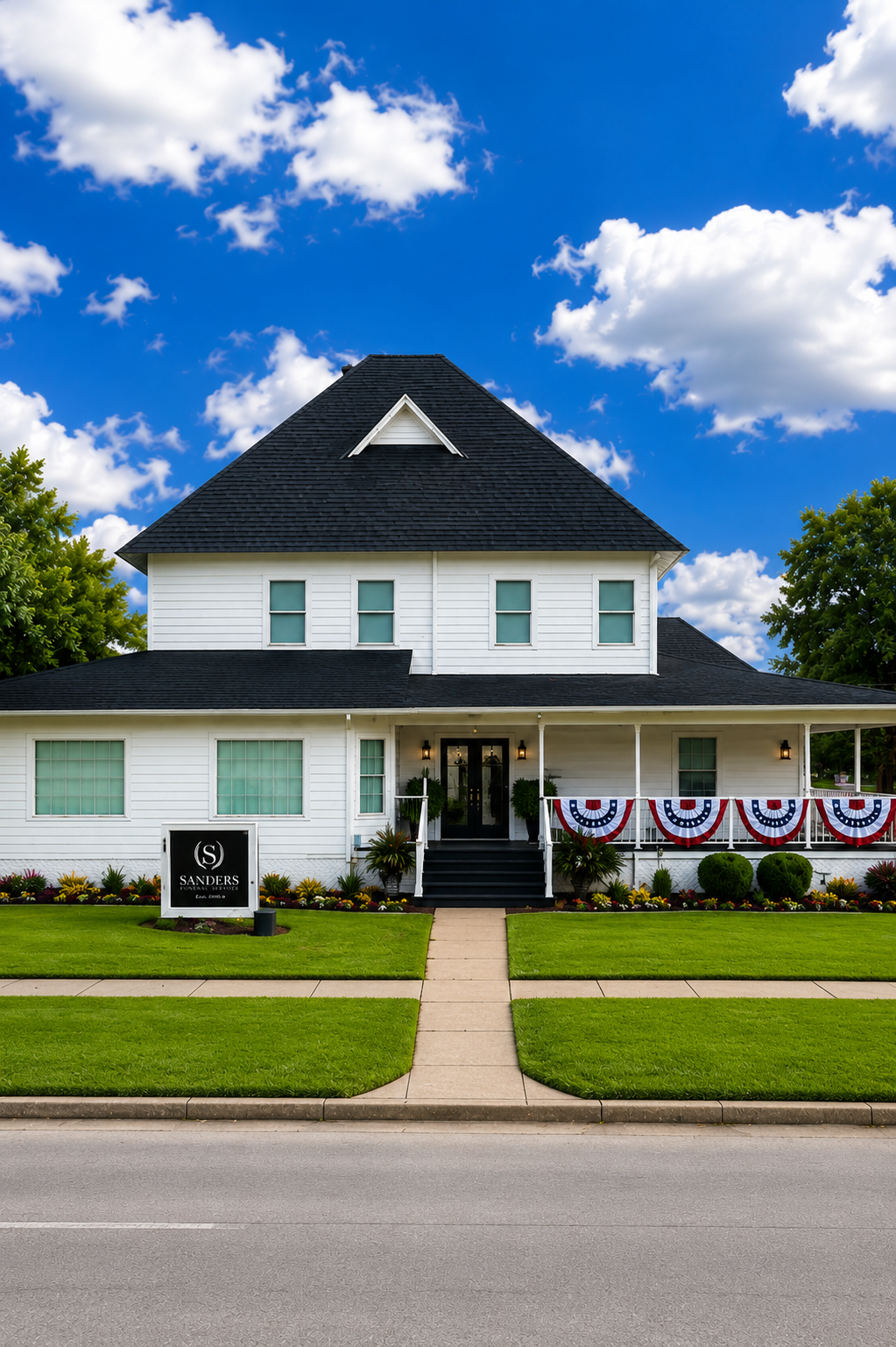 White two-story house with a black roof, front porch, and a large tree beside it.