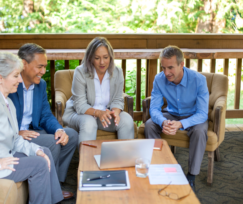 Four corporate employees, seating looking at a laptop in a cabin balcony.