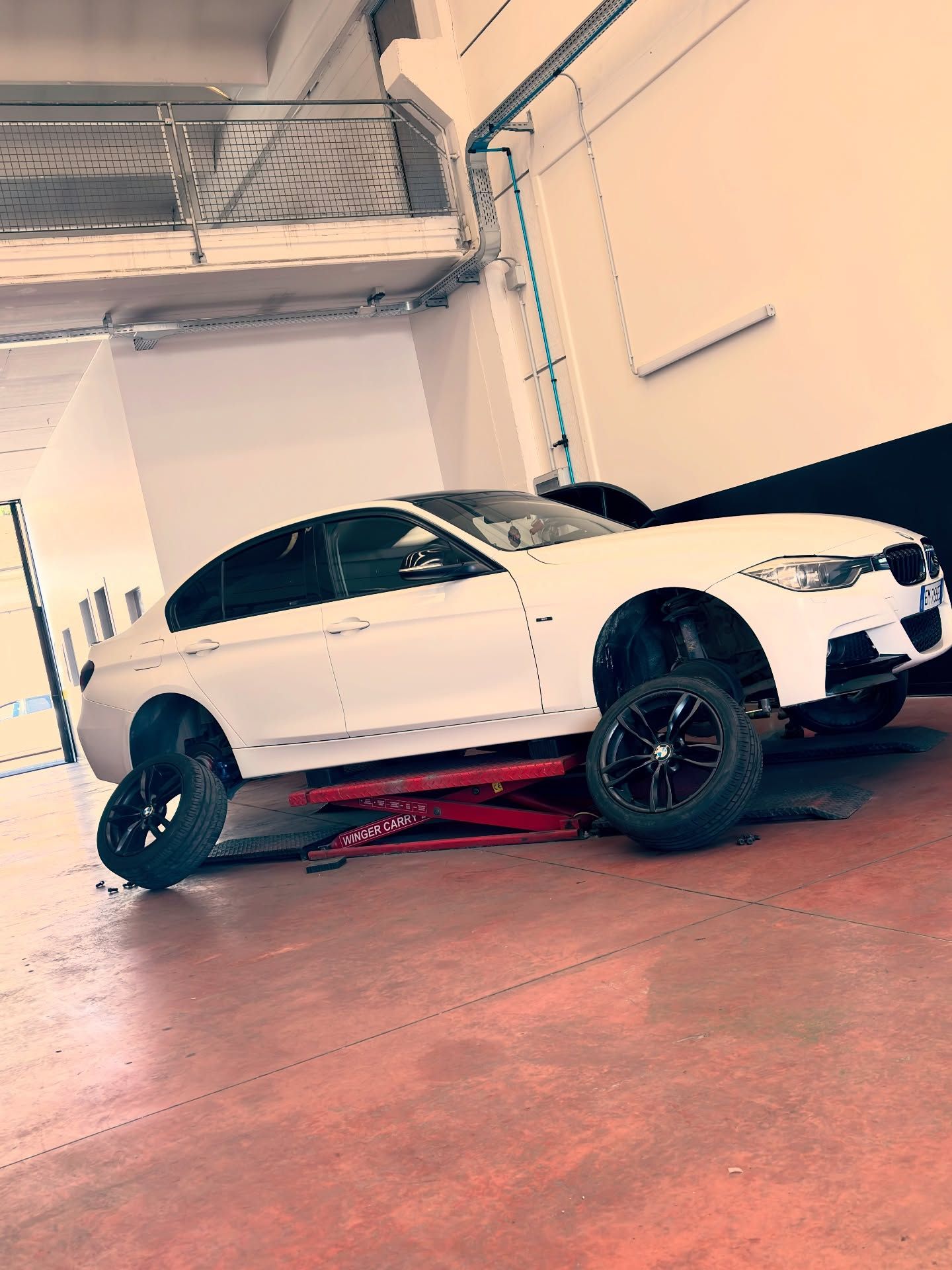 Berlina sportiva bianca su un sollevatore idraulico rosso all'interno di un'officina.