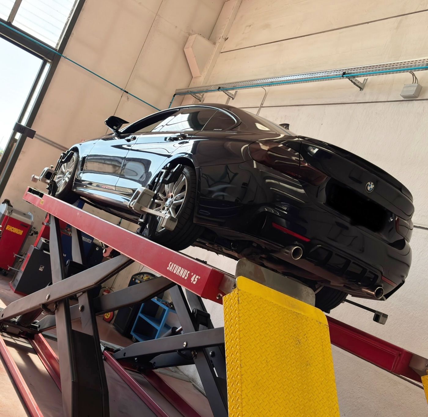 Auto sportiva nera sollevata su un ponte sollevatore rosso all'interno di un garage