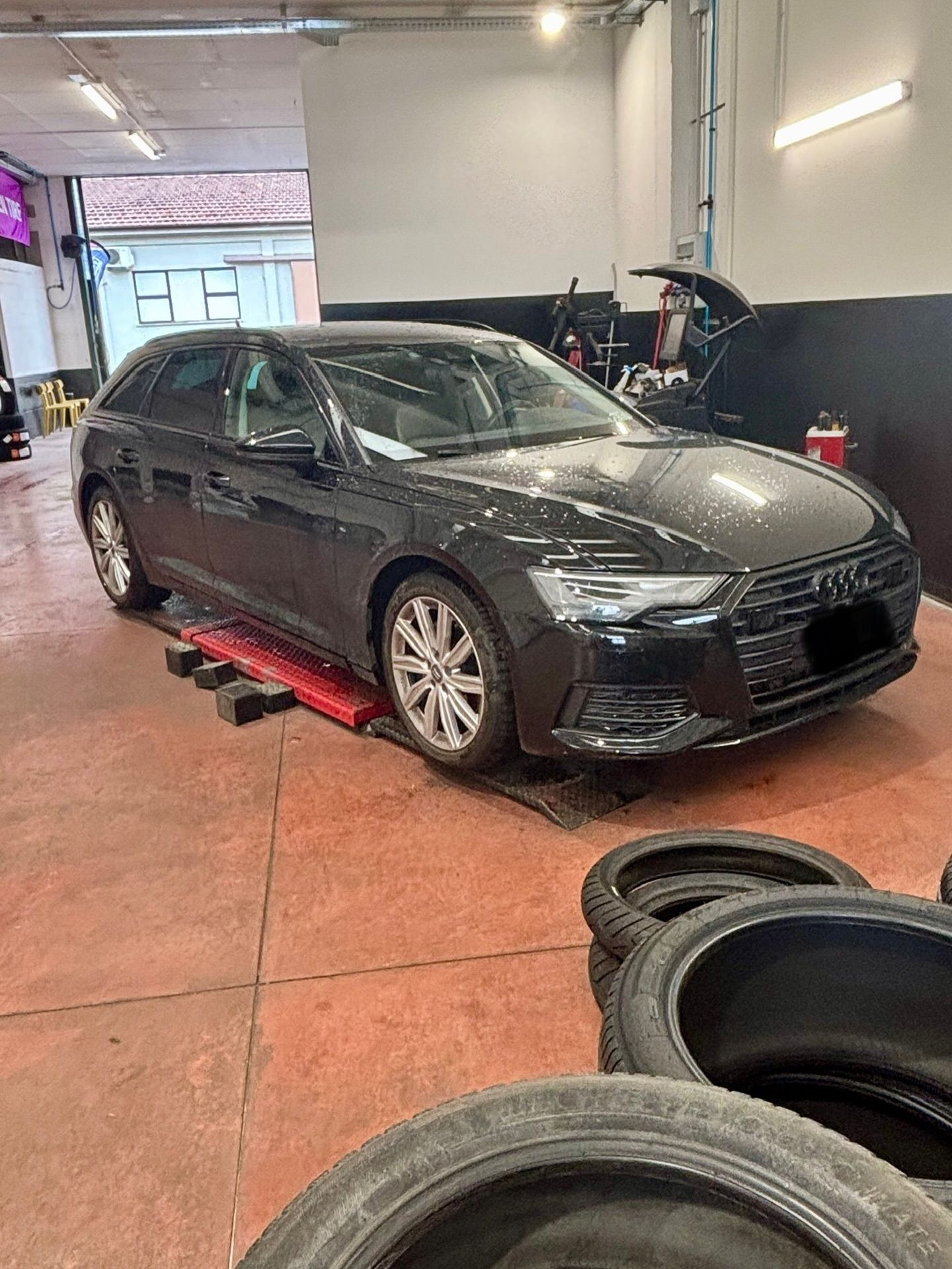 Berlina nera in un garage, vista frontalmente da sinistra, con pneumatici impilati in primo piano.