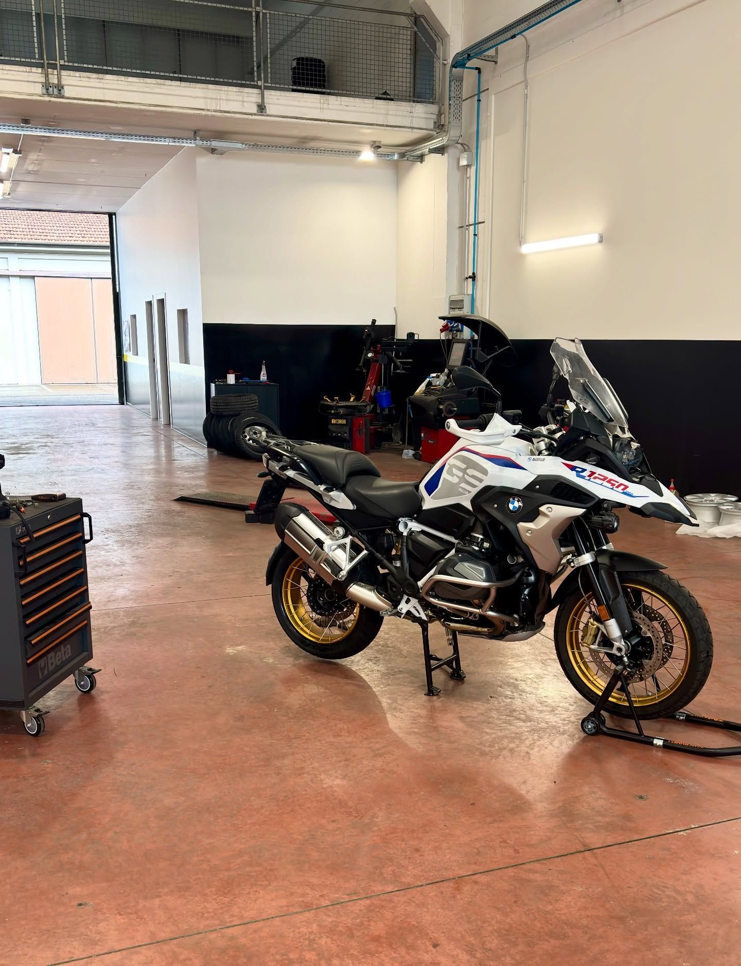 Motocicletta sportiva bianca in un garage con pavimento in cemento rosso e attrezzi nelle vicinanze.