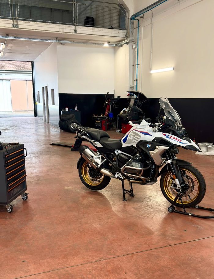Motocicletta sportiva bianca in un garage con pavimento in cemento rosso e attrezzi nelle vicinanze.