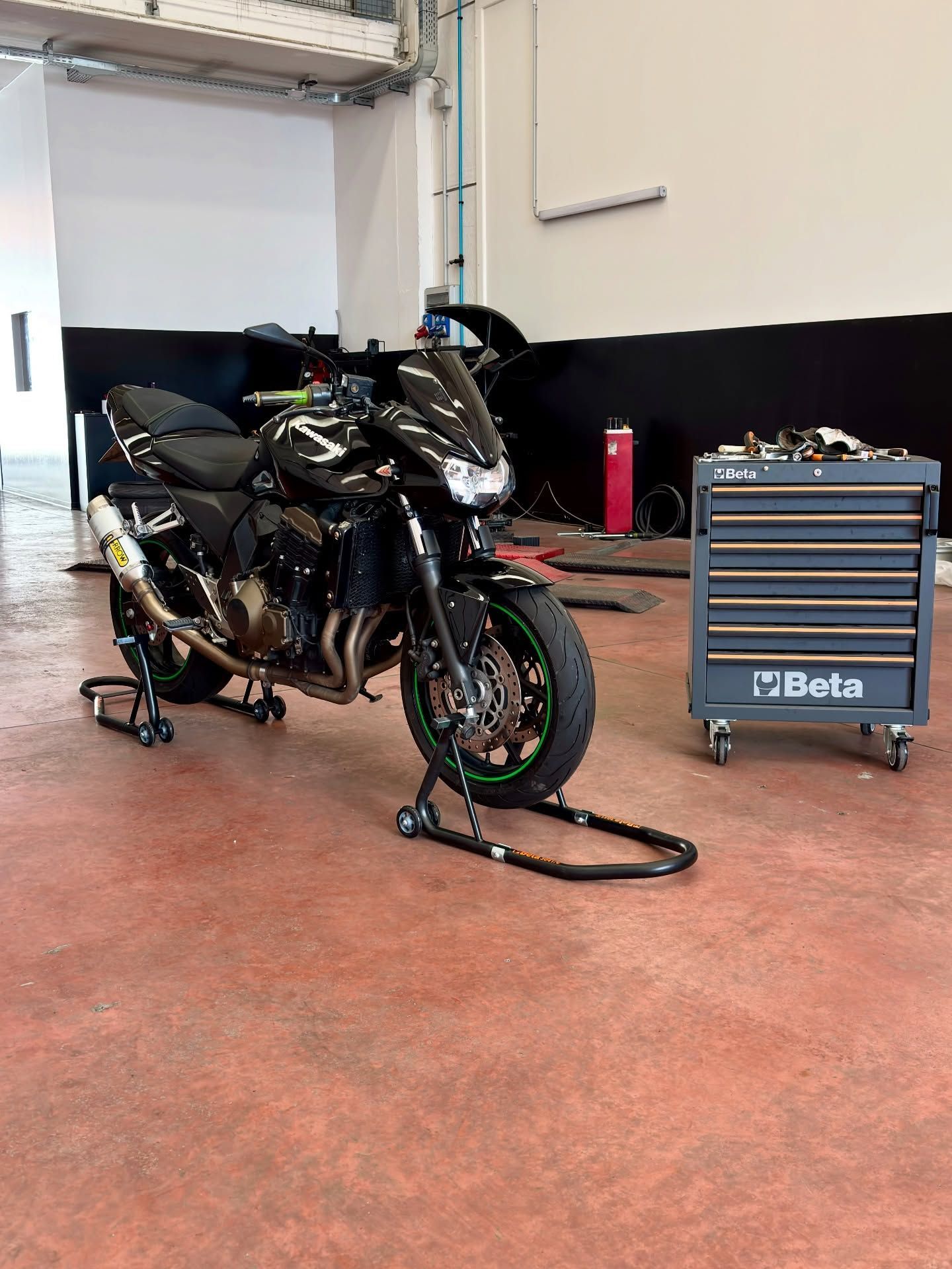 Una motocicletta sportiva nera in un'officina, con una cassetta degli attrezzi Beta blu nelle vicinanze.