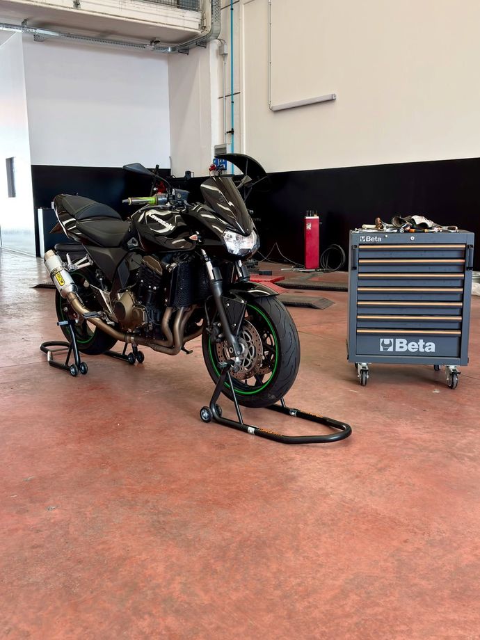 Una motocicletta sportiva nera in un'officina, con una cassetta degli attrezzi Beta blu nelle vicinanze.