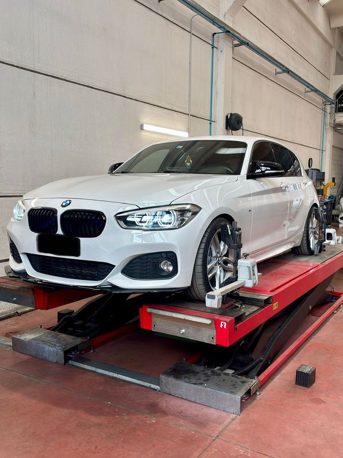 BMW bianca su un ponte sollevatore rosso in un'officina, ruote anteriori fissate con morsetti