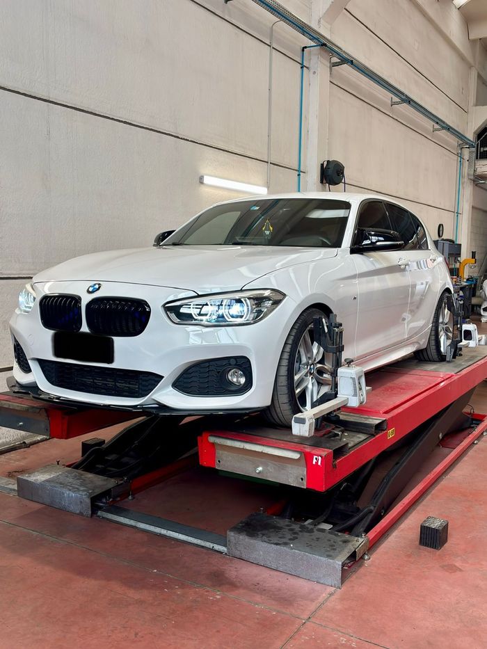 BMW bianca su un ponte sollevatore rosso in un'officina, ruote anteriori fissate con morsetti