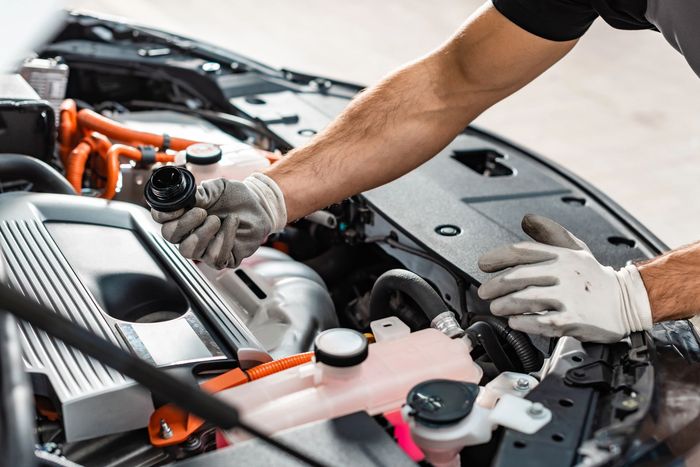 Meccanico al lavoro sotto il cofano di un'auto con le mani guantate e i componenti del motore visibili.