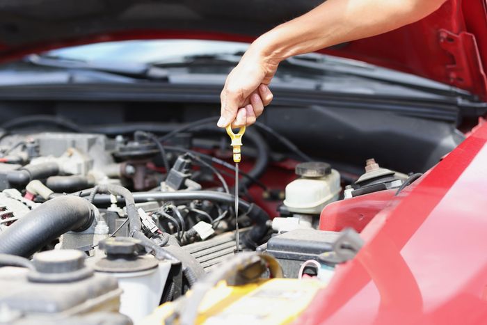 Una persona controlla l'olio motore con l'astina sotto il cofano aperto dell'auto.
