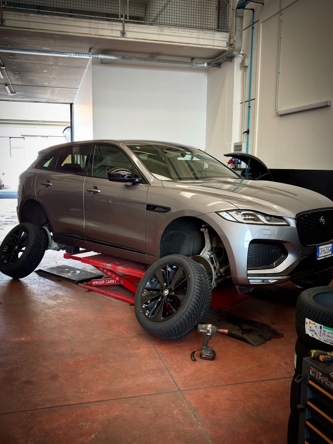 Un SUV grigio su un ponte sollevatore in un'officina, con le ruote smontate e gli attrezzi posizionati sotto.