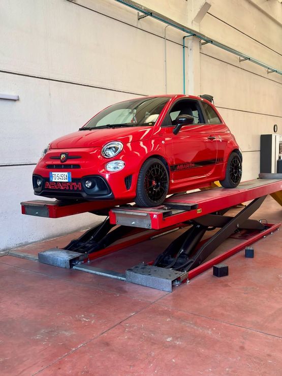 Auto compatta rossa su un ponte sollevatore rosso in un'officina.