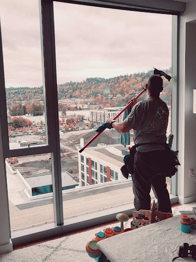 Professional window cleaner working on high-rise windows with a scenic view in Portland, Oregon.