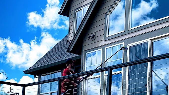 A man is cleaning the windows of a house with a hose.