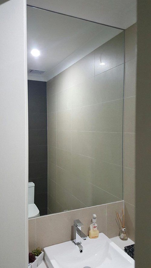 A modern bathroom featuring a rectangular wall-mounted mirror, white basin, chrome faucet, and neutral-toned wall tiles.