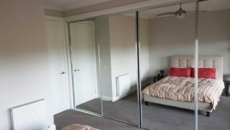 A bedroom featuring a bed with a striped quilt and red pillows, opposite mirrored sliding wardrobe doors.