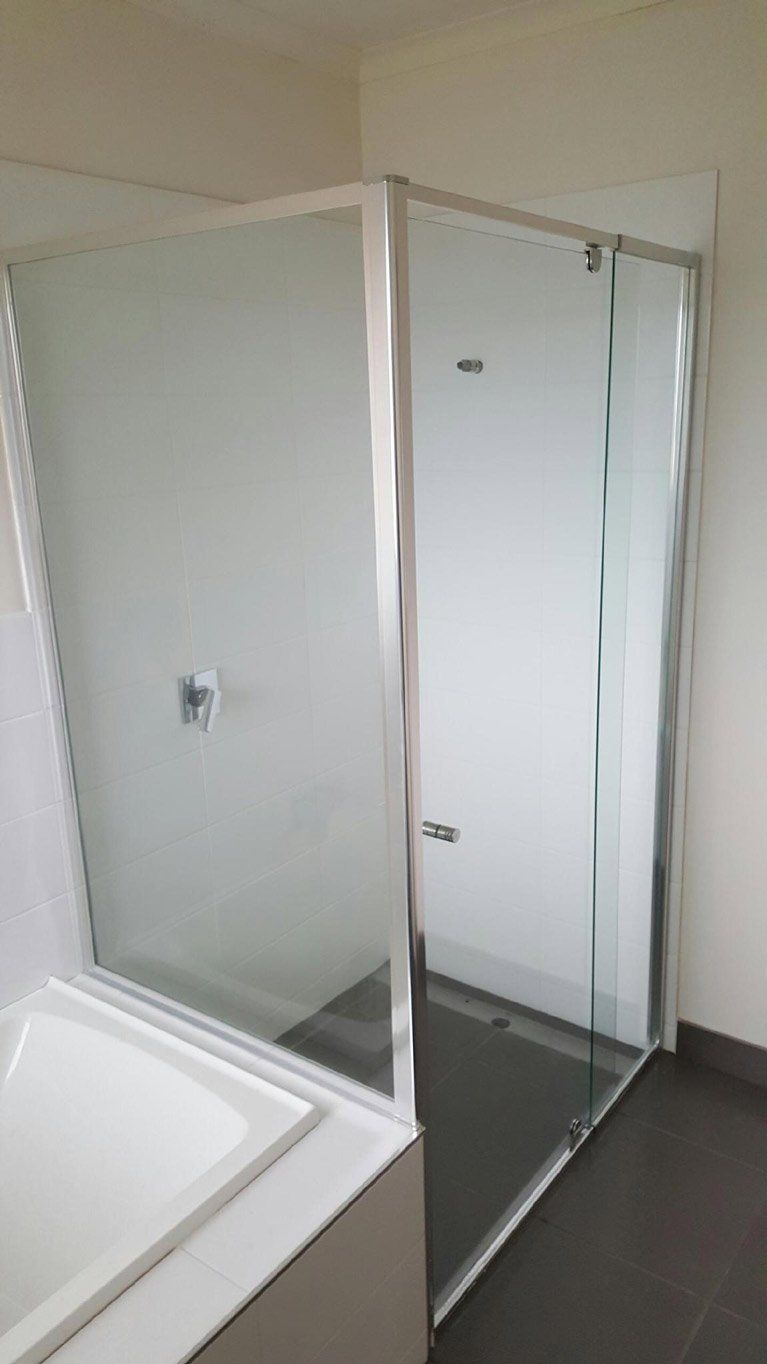 A glass shower enclosure with silver frames installed on a dark tile floor next to a white bathtub.