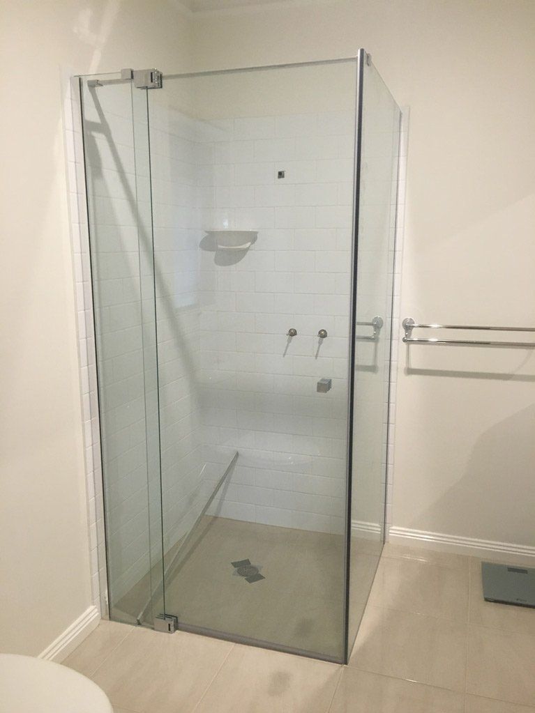 A modern, glass-enclosed shower stall with white tiled walls and neutral flooring in a bathroom.