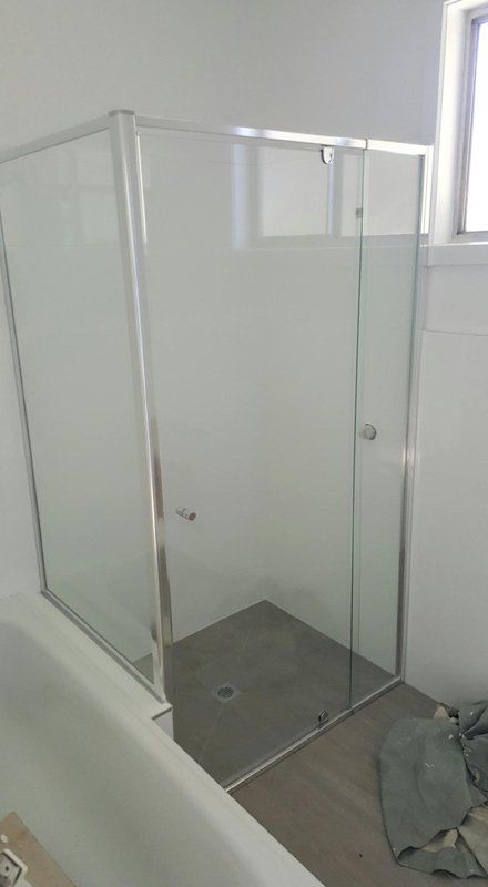 A modern, square glass shower enclosure with chrome frames, installed in a bathroom next to a bathtub.