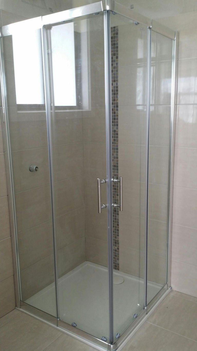 A modern corner shower enclosure with a white base, glass panels, and a chrome frame in a tiled bathroom.