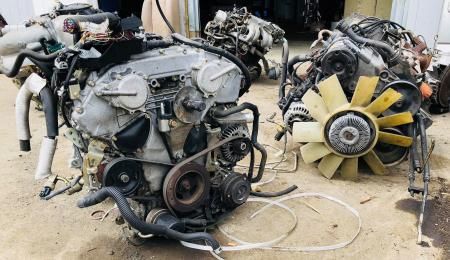 Three dismantled car engines on the ground, various parts visible, one with a yellow fan.
