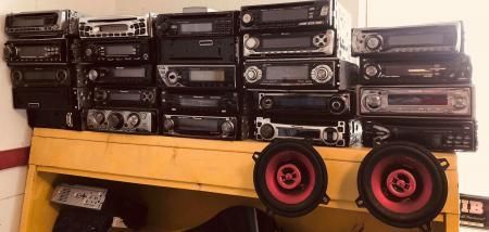 A shelf is filled with car stereos, and two speakers with red accents are at the front.