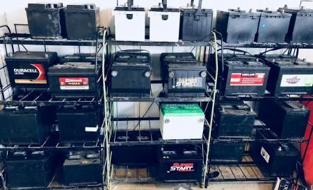 Metal shelving unit displaying numerous car batteries of varying brands and sizes.