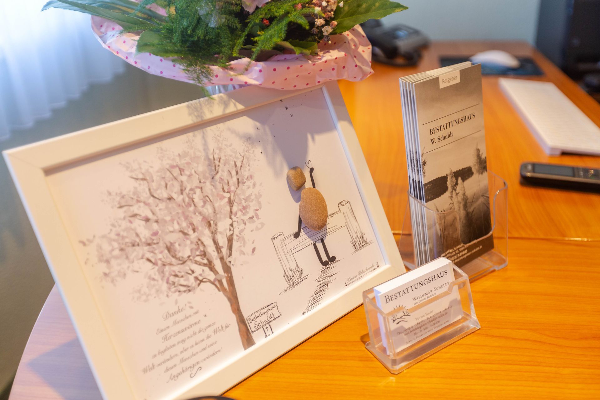Gerahmte Kunst, Blumenstrauß, Broschüren und Visitenkarten auf einem Schreibtisch.