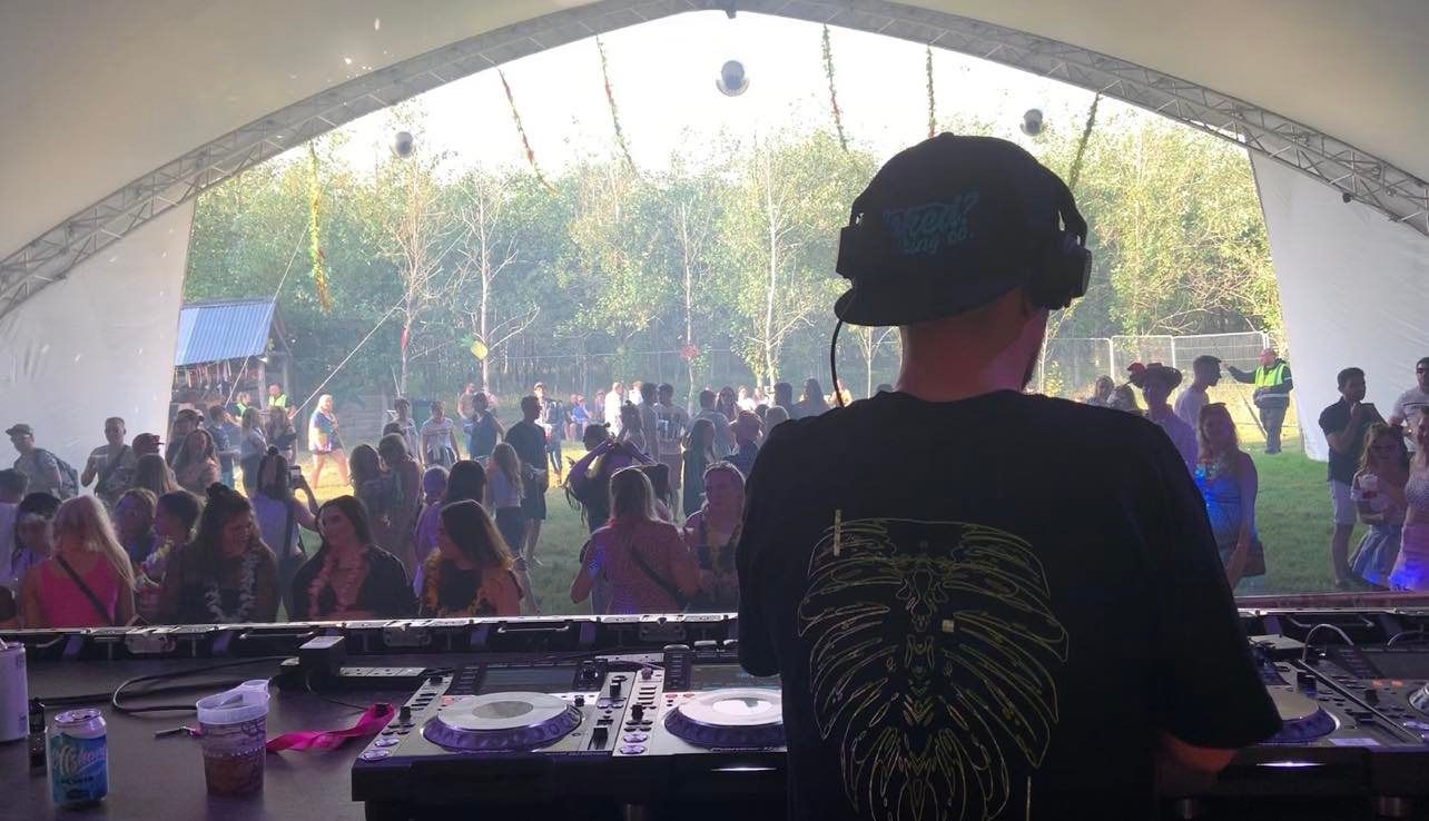 A dj is playing music in front of a crowd at a festival.