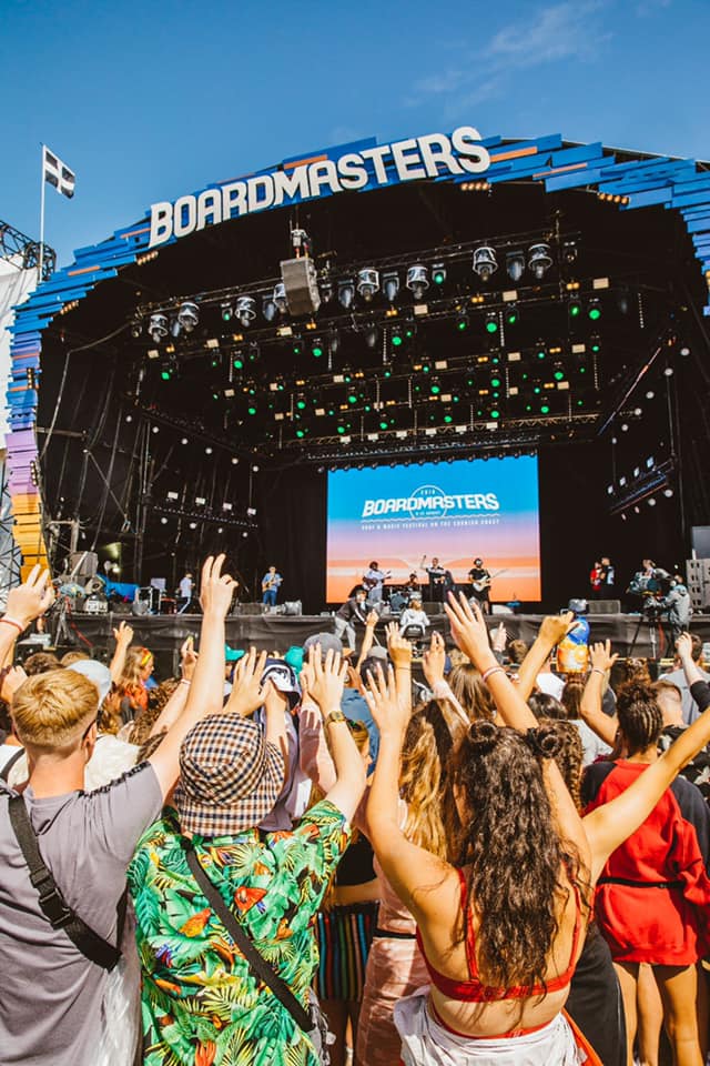 A crowd of people are standing in front of a stage at a music festival.