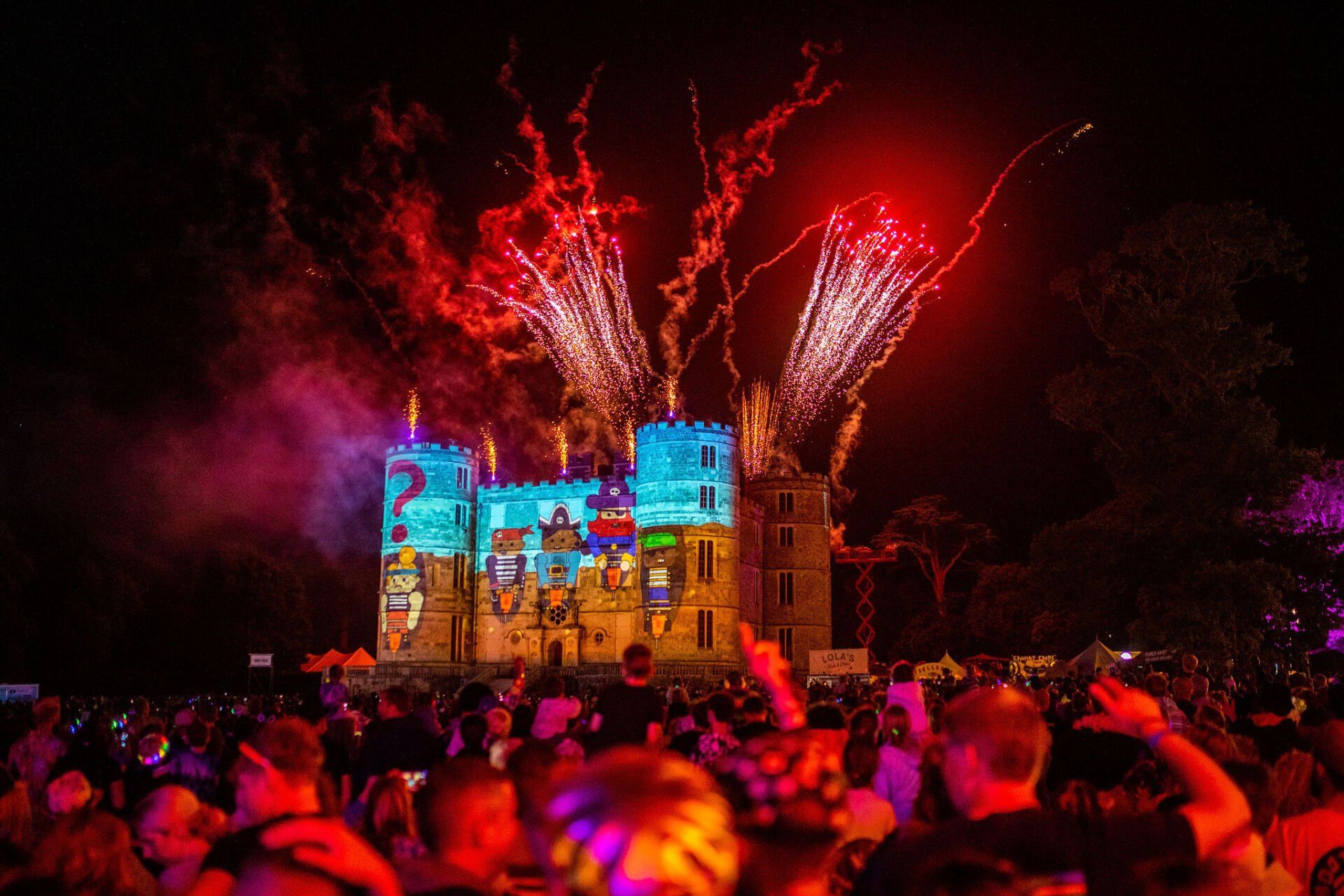 A crowd of people are watching fireworks in front of a castle.
