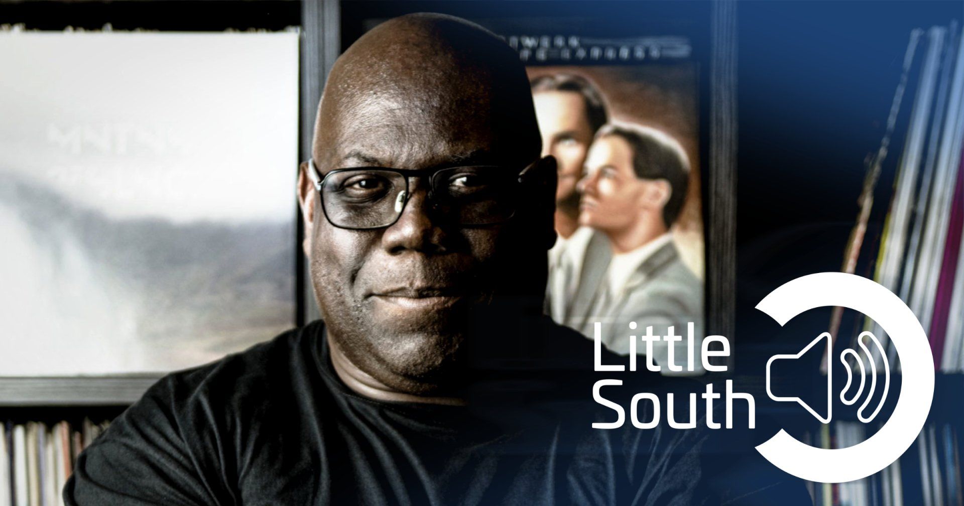 A man wearing glasses stands in front of a little south logo