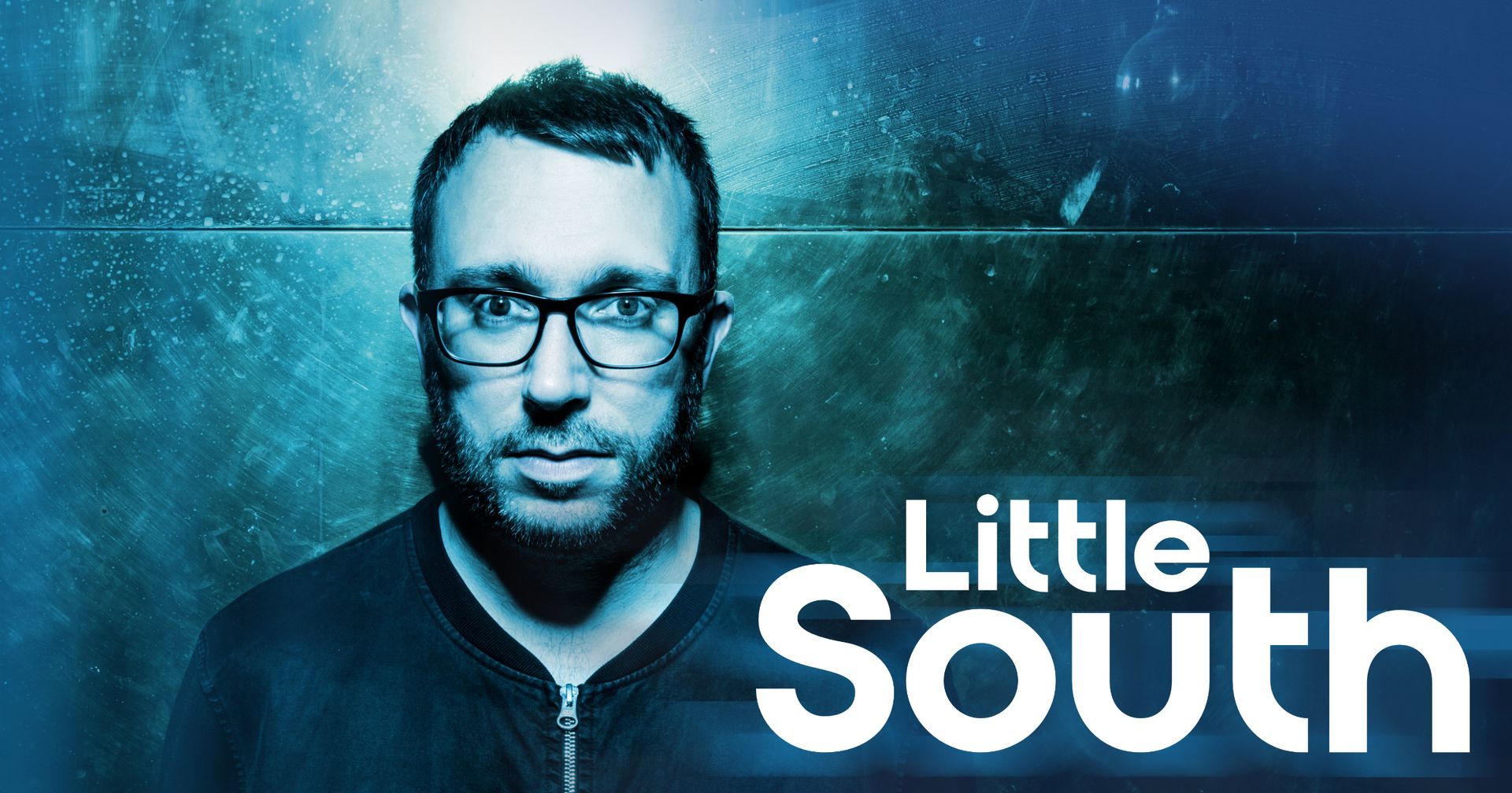 A man with glasses stands in front of a sign that says little south