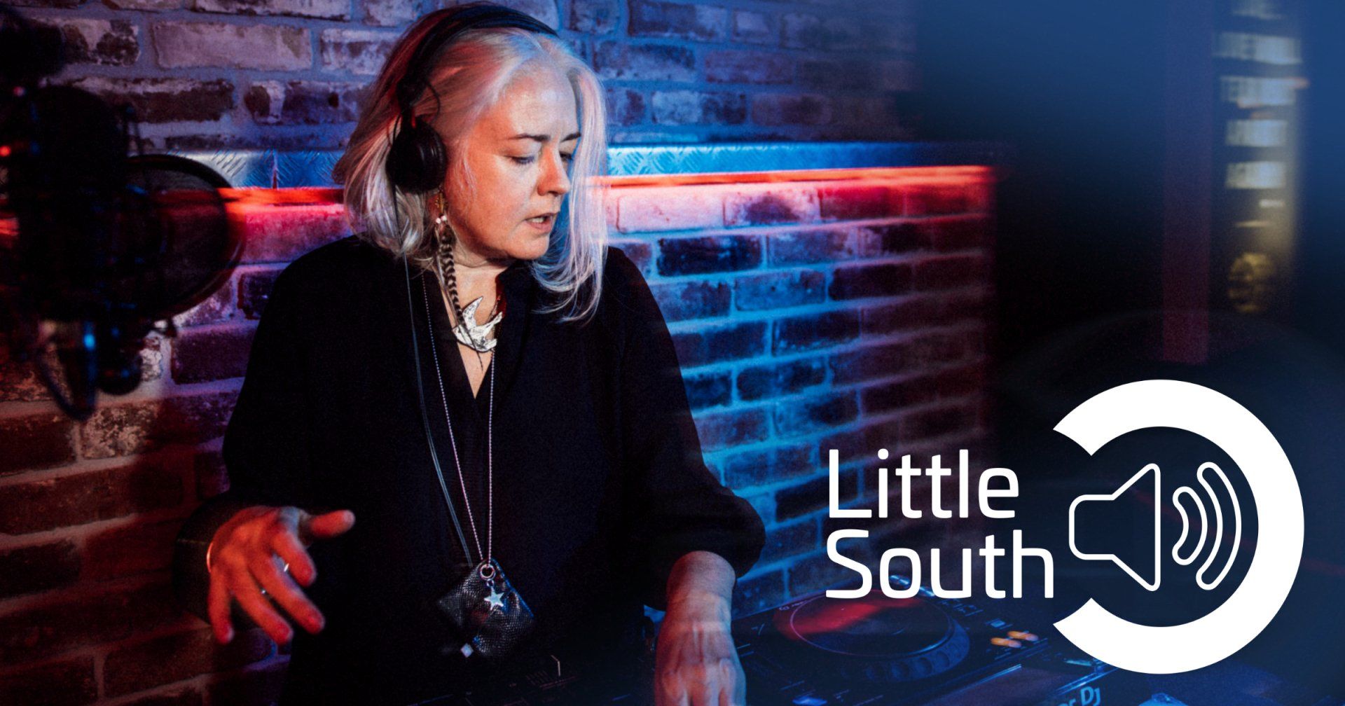 A woman wearing headphones is playing music in front of a brick wall.