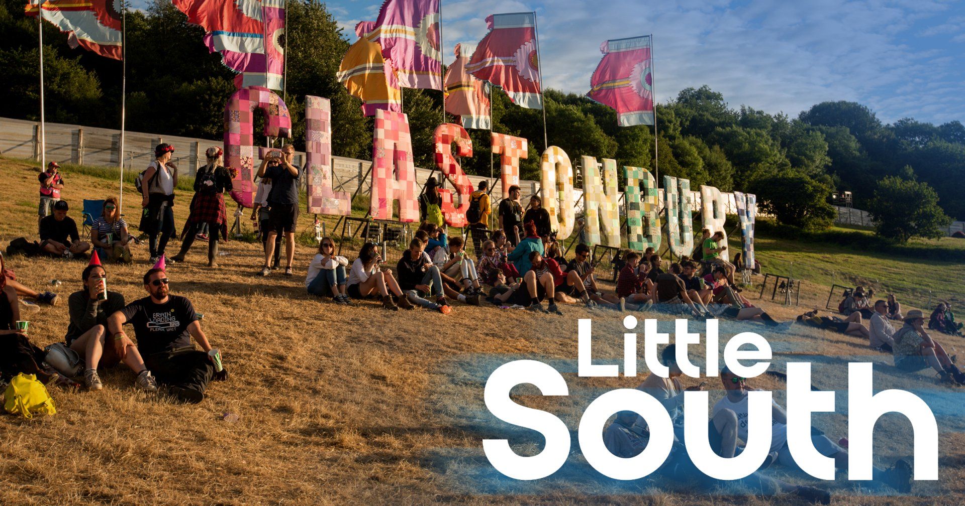 A group of people are sitting in a field with a sign that says little south.