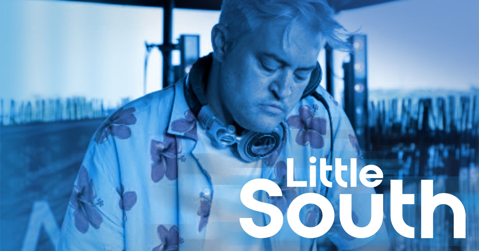 A man wearing headphones is standing in front of a blue background with the words `` little south ''.