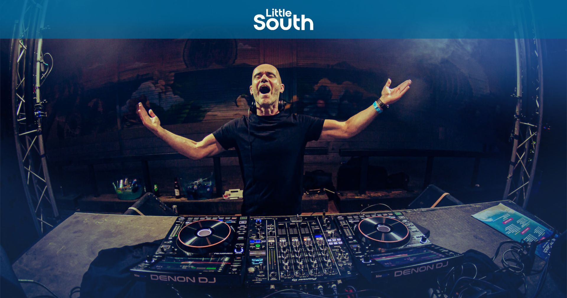 A man is standing in front of a dj booth with his arms outstretched.