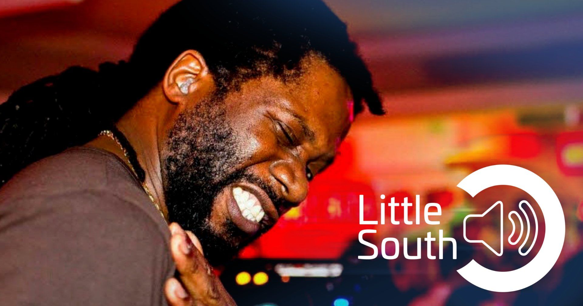 A man with dreadlocks is smiling in front of a little south logo