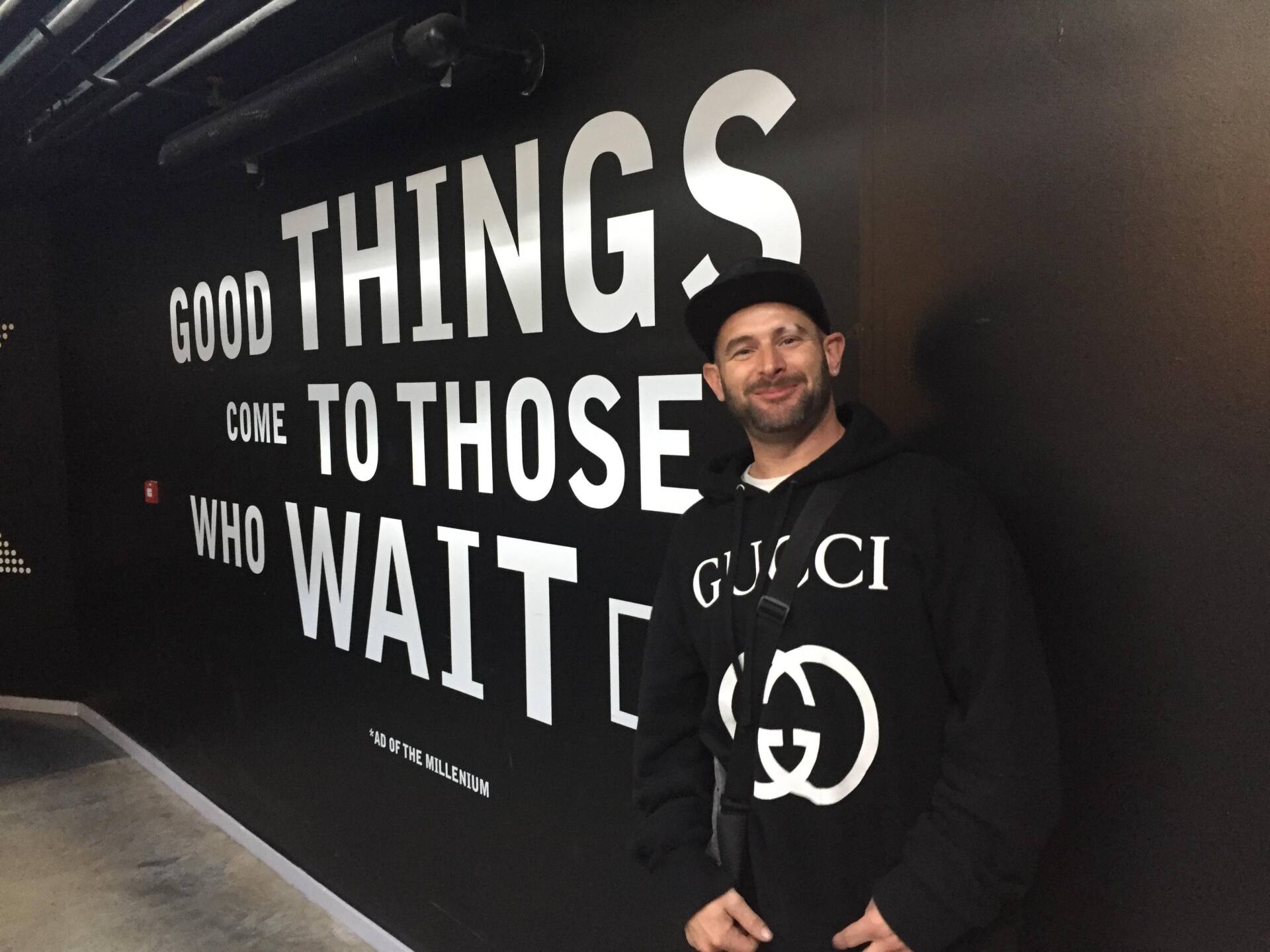 A man stands in front of a wall that says good things come to those who wait