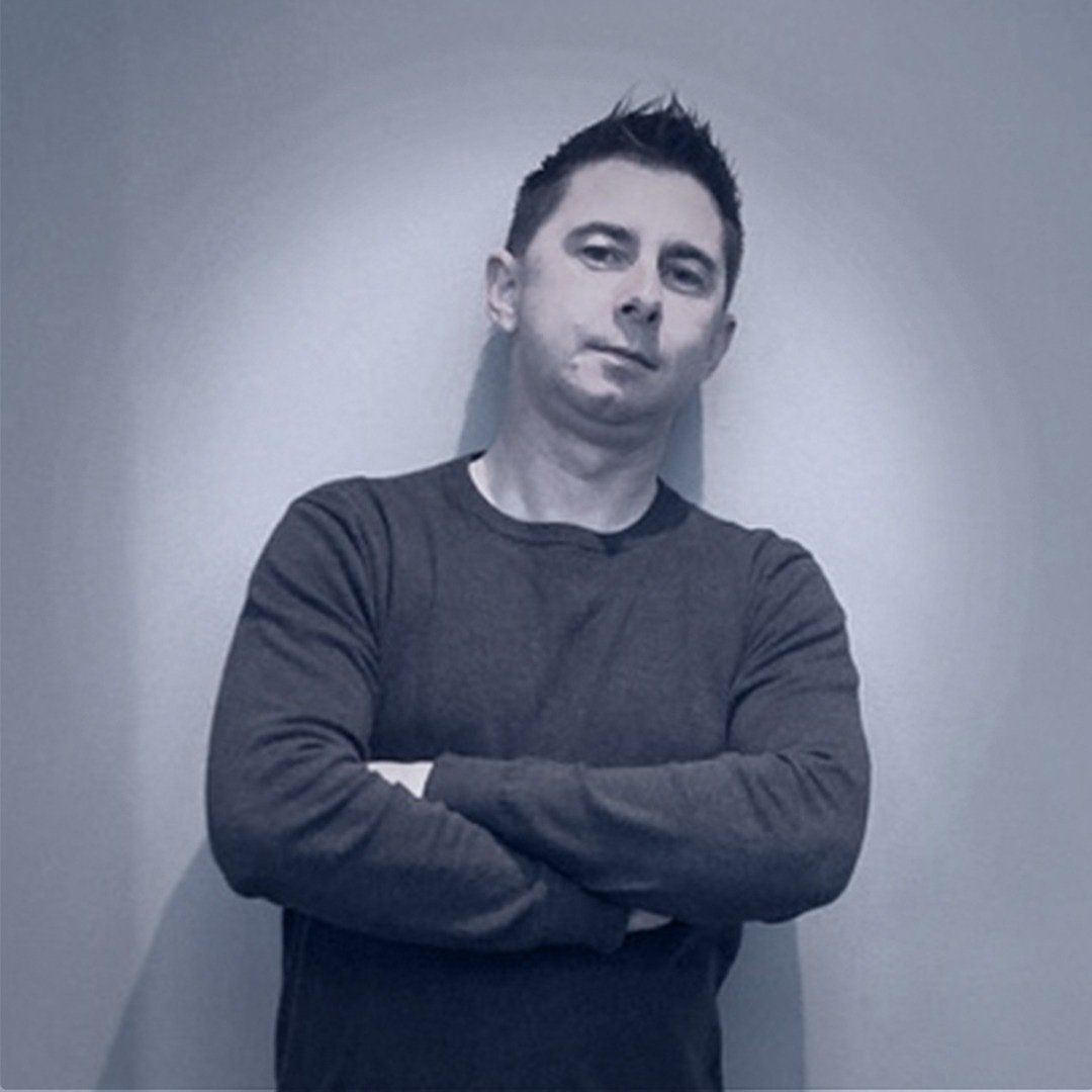 A man is standing with his arms crossed in front of a wall.
