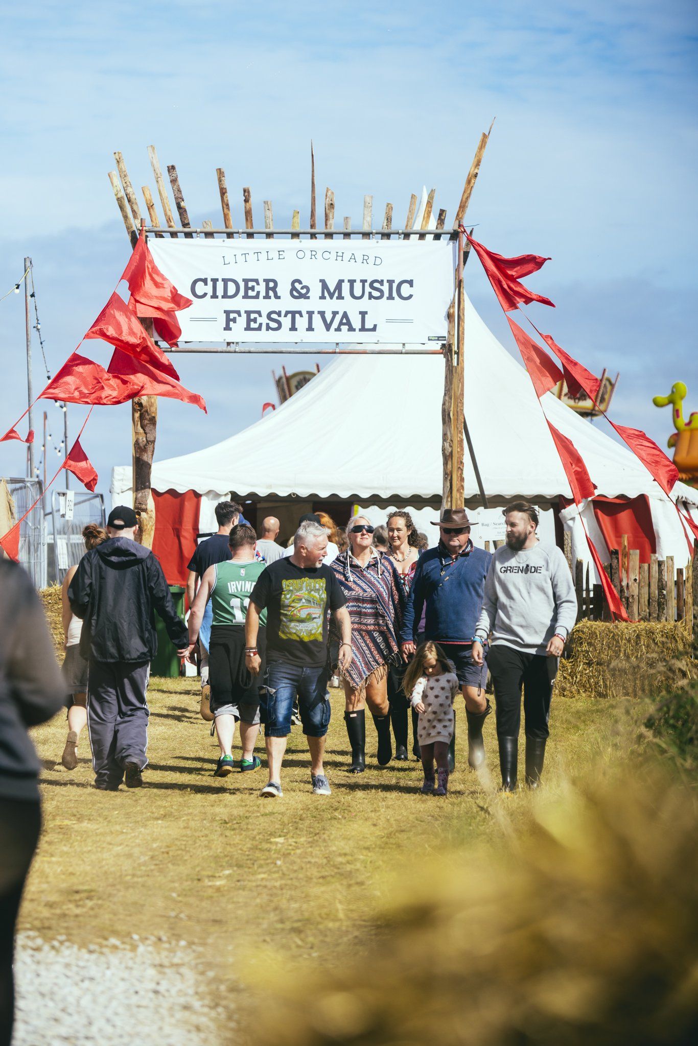 A group of people are walking towards a tent at a cider and music festival.