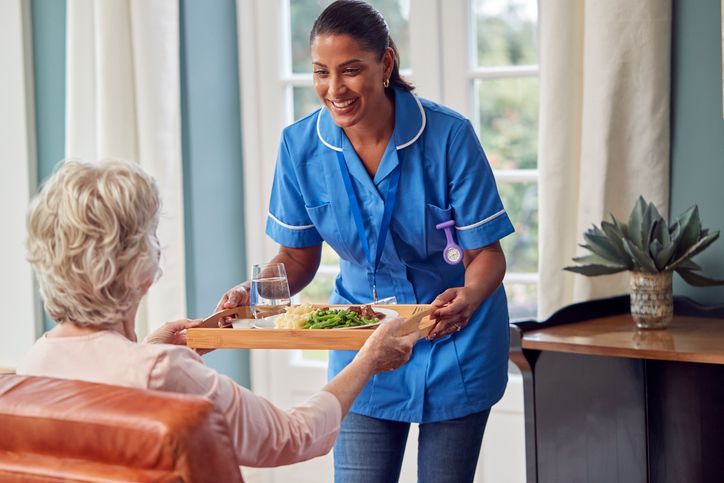A nurse is serving food to an elderly woman in a living room.