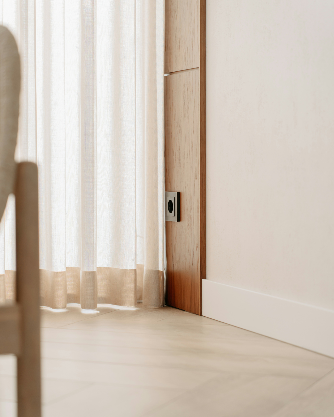 Suelo de madera clara, cortinas beige y una pared blanca con un pequeño panel de puerta de madera.
