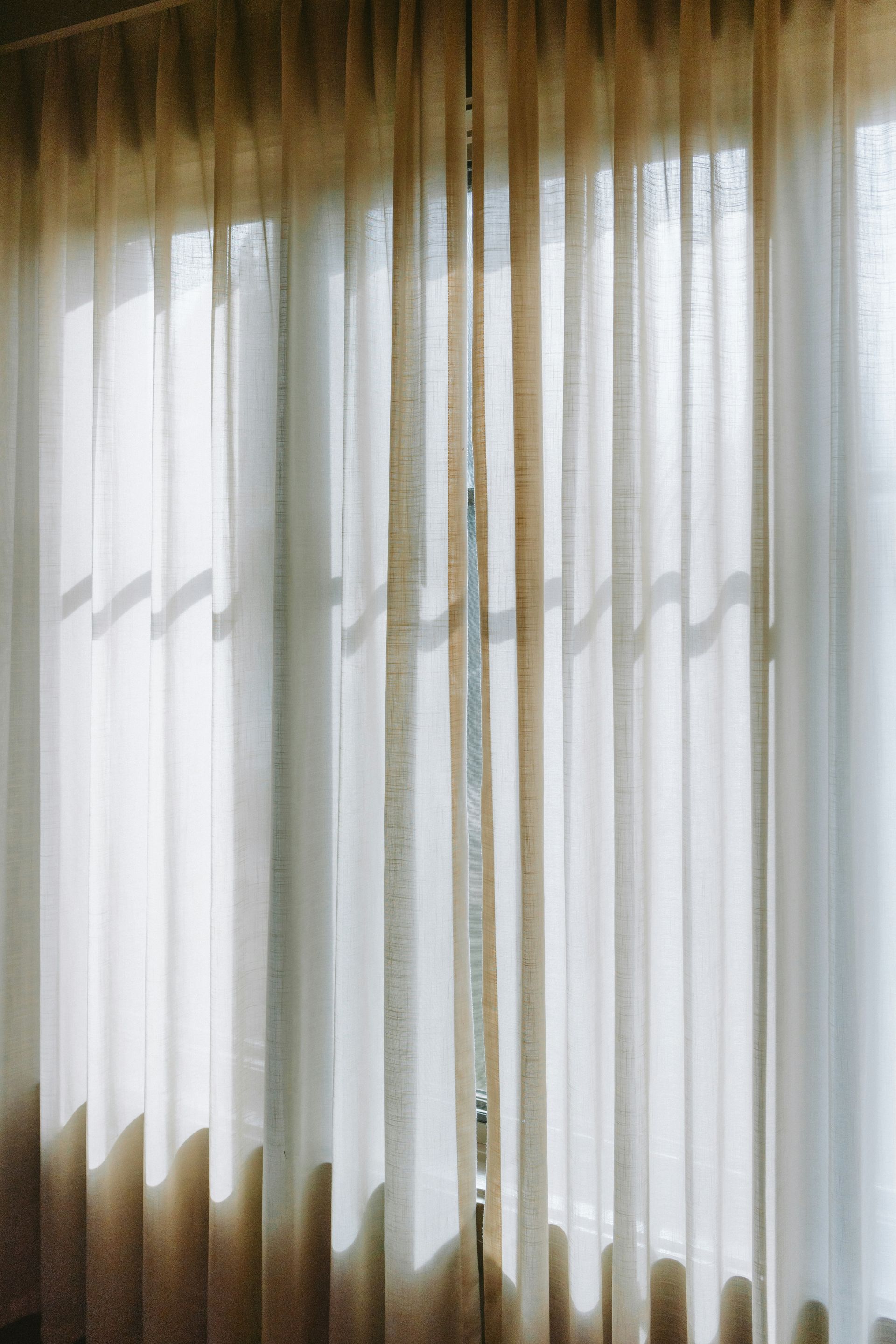 Cortinas transparentes que brillan con la luz del día, proyectando suaves sombras sobre la ventana.