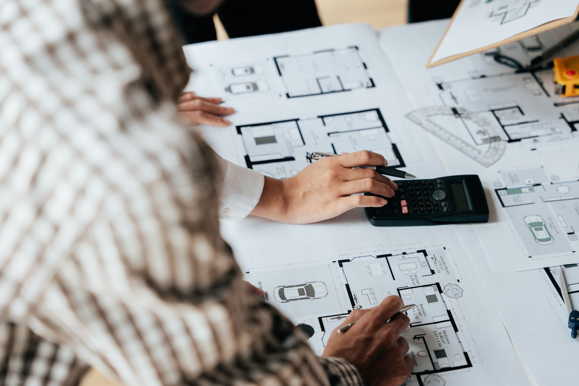 Hands using calculator and pen on blueprints of a building layout.