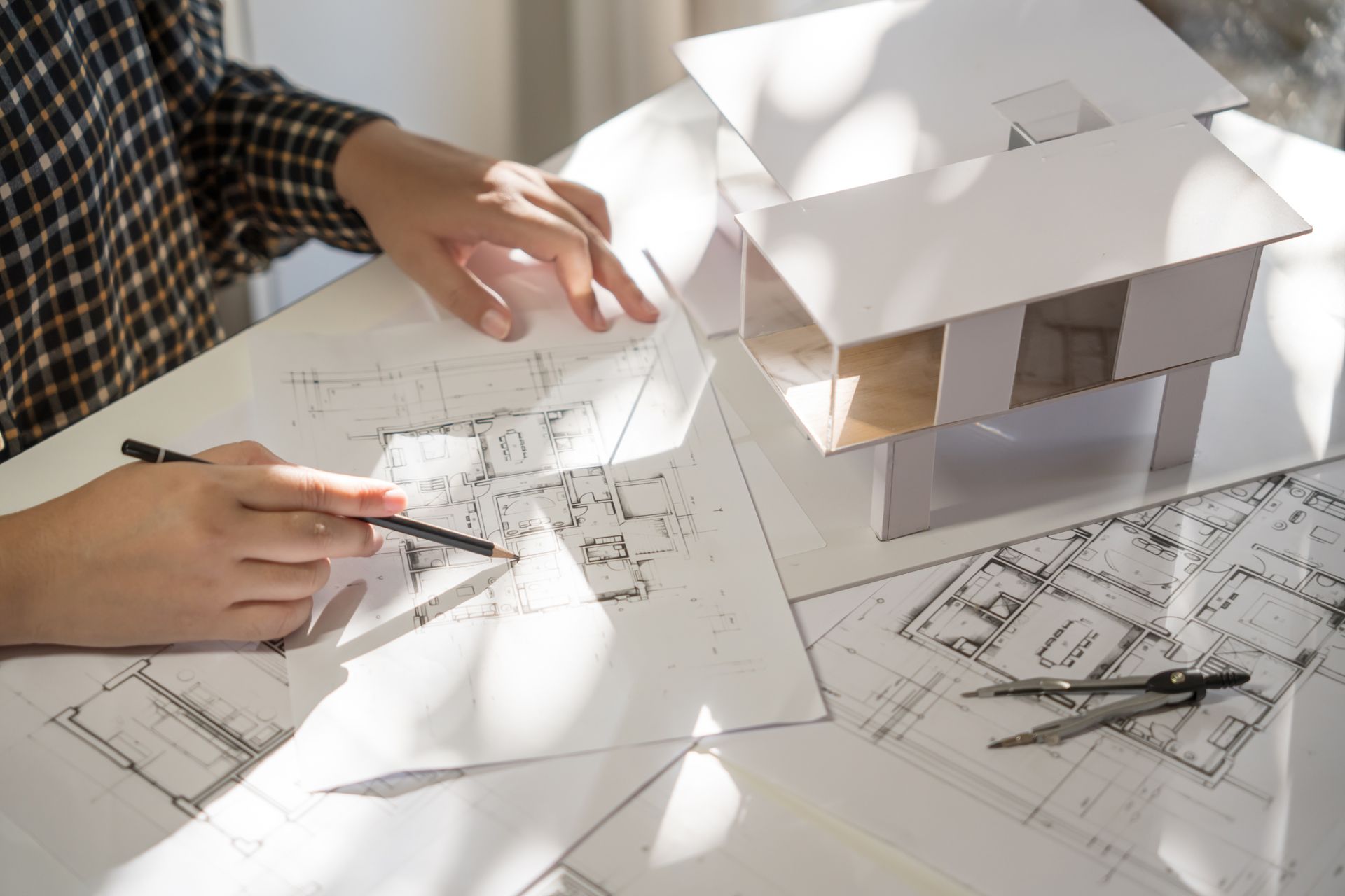 Architect sketching blueprints with a model house nearby.