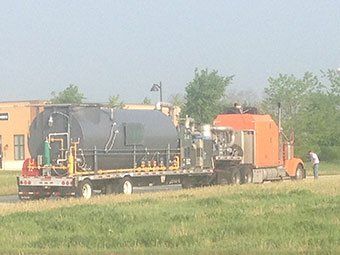 An orange semi truck is pulling a large black tank on a trailer