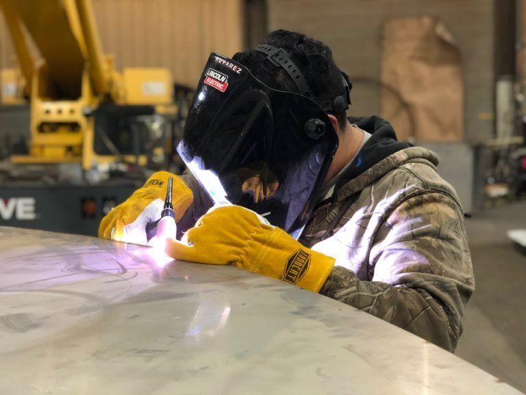 A man wearing a welding mask and yellow gloves is welding a piece of metal.