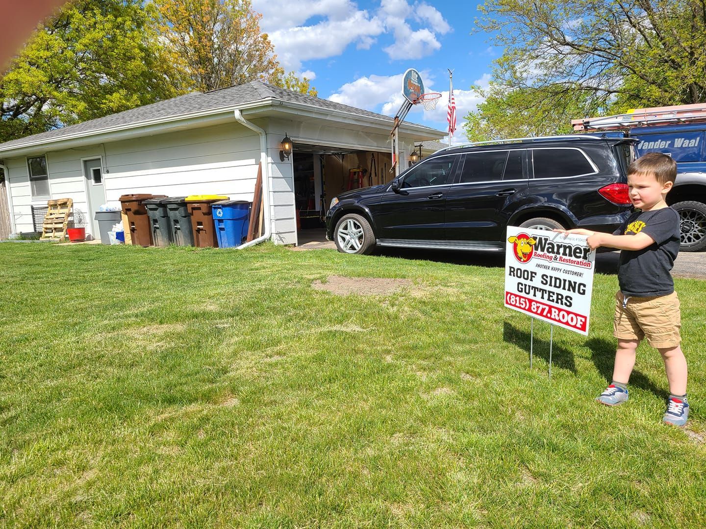 A child standing on a grassy lawn next to a yard sign for a roofing company, with a house and black SUV in the background.