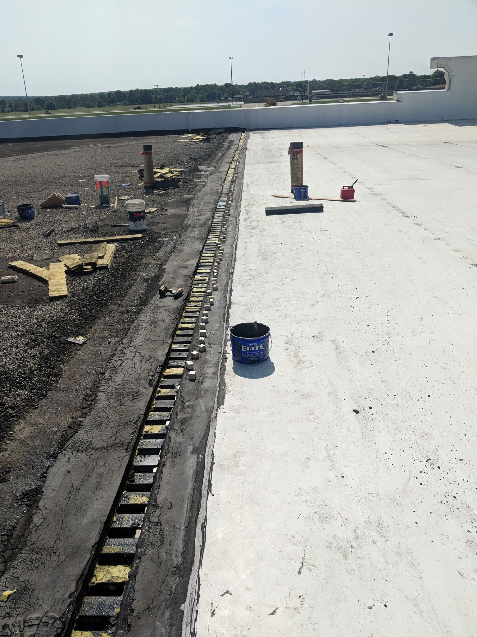 A rooftop undergoing construction, showing a black drainage channel dividing a gravel area and a white membrane surface.